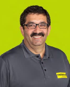 Man with glasses and moustache wearing dark Freshco shirt on green background